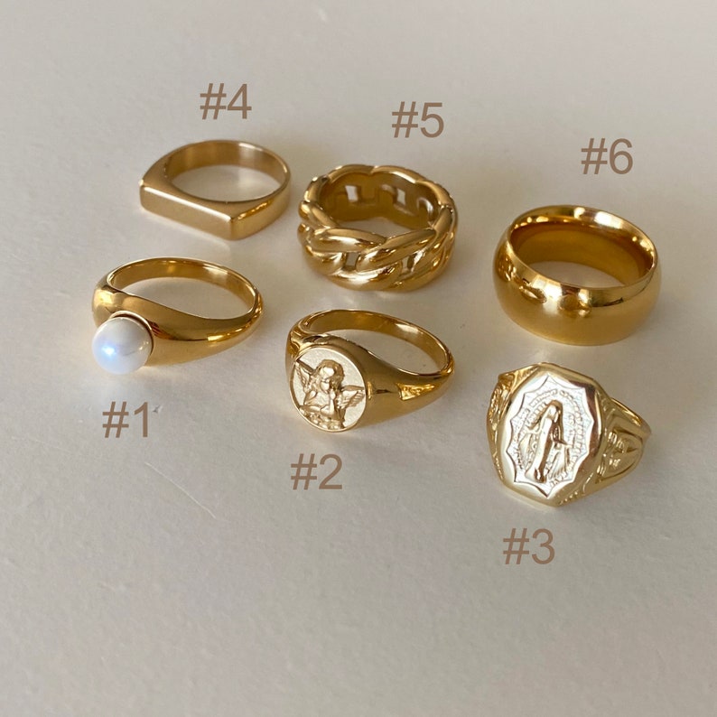 May include: Ten gold rings with different designs, including a ring with a pearl, a ring with an angel, a ring with a religious figure, a ring with a braided design, and a simple band ring.