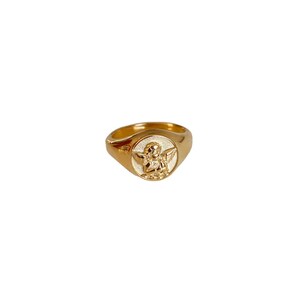 May include: A gold signet ring with a white enamel angel design.