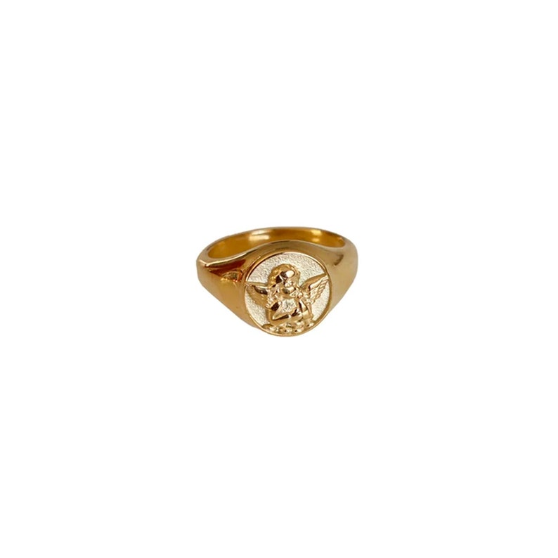 May include: A gold signet ring with a white enamel angel design.
