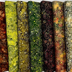 May include: A collection of fabric rolls in various colors, including brown, yellow, green, and burgundy. Each roll features a repeating pattern of white circles, creating a textured appearance. The fabrics appear to be batik or hand-dyed.