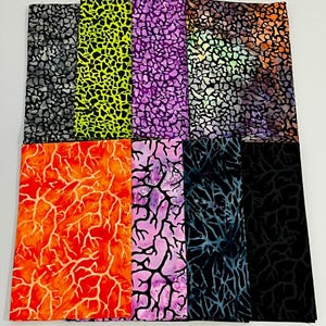 May include: A collection of fabric pieces in various colors and patterns. The fabrics feature designs with irregular shapes and branch-like patterns in shades of gray, neon green, purple, orange, pink, and black. The fabrics are neatly folded.