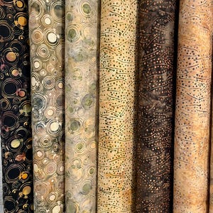 May include: A collection of fabric rolls with various patterns. The fabrics feature designs of circles and dots in shades of black, brown, tan, and green. The rolls are vertically oriented, showcasing the different patterns and colors.