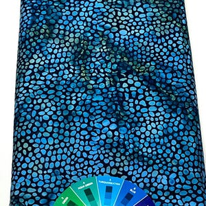 May include: A bolt of fabric with a blue and black pebble-like pattern. The fabric has a color palette with shades of blue, aqua, and green. A color wheel is in the foreground, showing color variations.