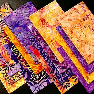 May include: An assortment of colorful fabric squares with botanical patterns. The fabrics feature shades of orange, yellow, and purple, with leaf and fern designs. The arrangement is angled, showcasing the variety of patterns and colors.