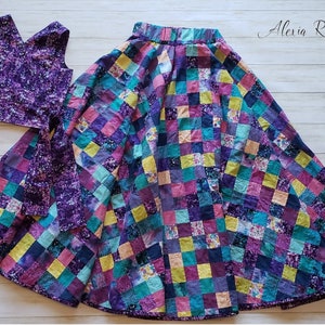 May include: A purple and teal patchwork skirt with a matching purple top. The skirt is made of many different fabrics and has a gathered waist. The top is sleeveless and has a V-neck.
