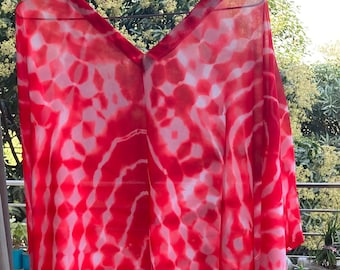May include: A flowing, red and white tie-dye patterned garment. The fabric drapes loosely, with a V-neckline. The design features a repeating pattern of red and white shapes, creating a vibrant and eye-catching effect. The garment appears lightweight and airy.