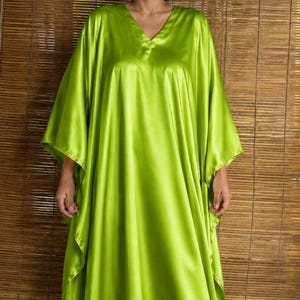 May include: A floor-length lime green kaftan dress featuring a V-neckline and wide, flowing sleeves. The garment is crafted from a smooth, lustrous fabric with a satin-like finish that drapes loosely from the shoulders to the floor in a relaxed fit.