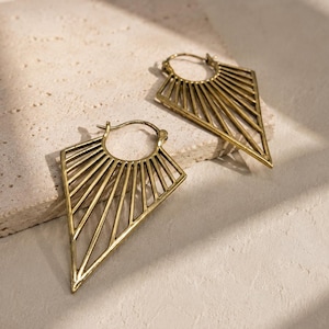 May include: A pair of gold-toned hoop earrings featuring a geometric, fan-like design that extends into a sharp, pointed triangle shape. The earrings are constructed with thin, radiating metal bars that create an open, airy structure.