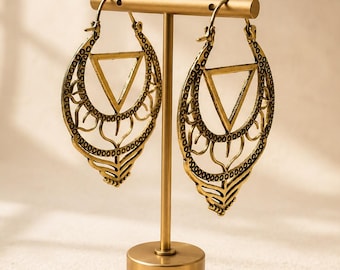 May include: A pair of antique gold-toned hoop earrings featuring an intricate filigree design with a central triangle cutout. The earrings are suspended from a T-shaped metal display stand with a circular base, showcasing the detailed metalwork.