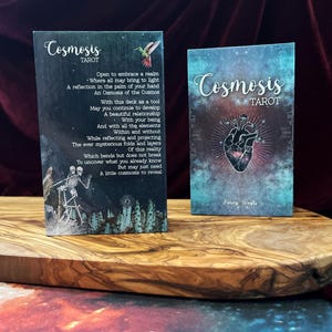 May include: Two rectangular tarot card boxes titled Cosmosis Tarot. The left box features a poem, a hummingbird, and skeleton figures. The right box displays a central anatomical heart illustration with radiating lines against a teal and purple nebula background.