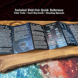 May include: A black, multi-panel fold-out quick reference guide for the Cosmosis Tarot deck. The paper features white text, celestial graphics, and a heart illustration. It includes sections on card keywords, reading spreads, and major arcana.
