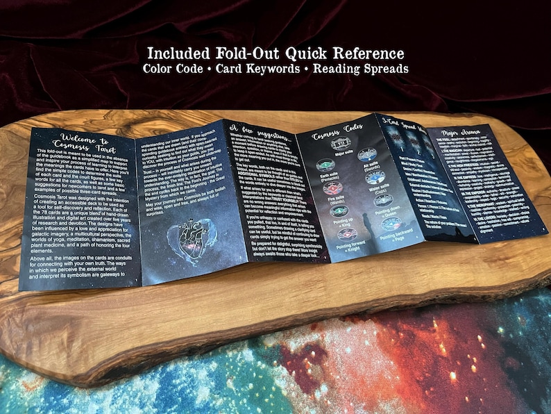 May include: A black, multi-panel fold-out quick reference guide for the Cosmosis Tarot deck. The paper features white text, celestial graphics, and a heart illustration. It includes sections on card keywords, reading spreads, and major arcana.