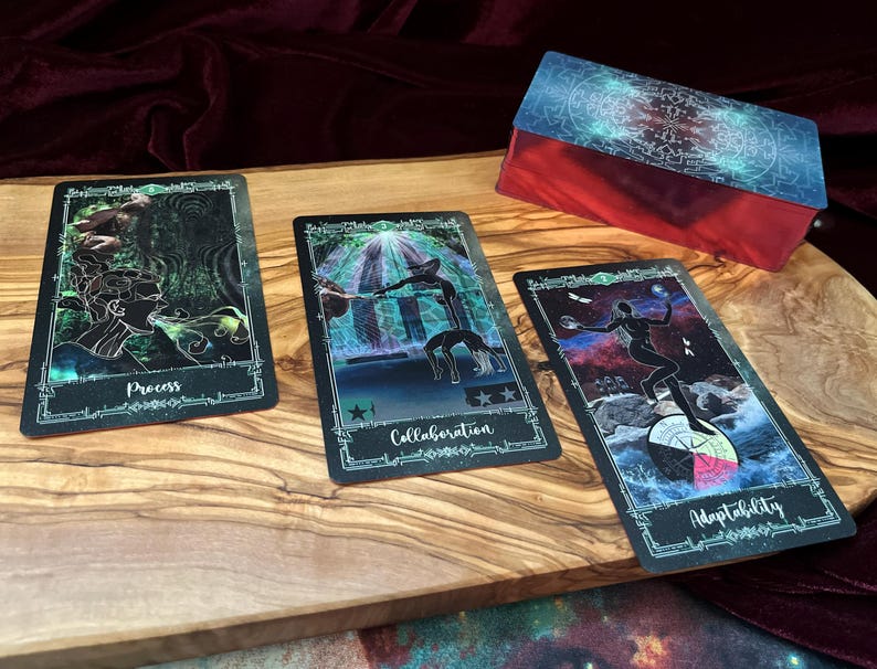 May include: Three rectangular tarot cards with dark, cosmic-themed illustrations and a matching deck box. The cards feature the words Process, Collaboration, and Adaptability in white script. Each card has a decorative border and vibrant, colorful imagery.