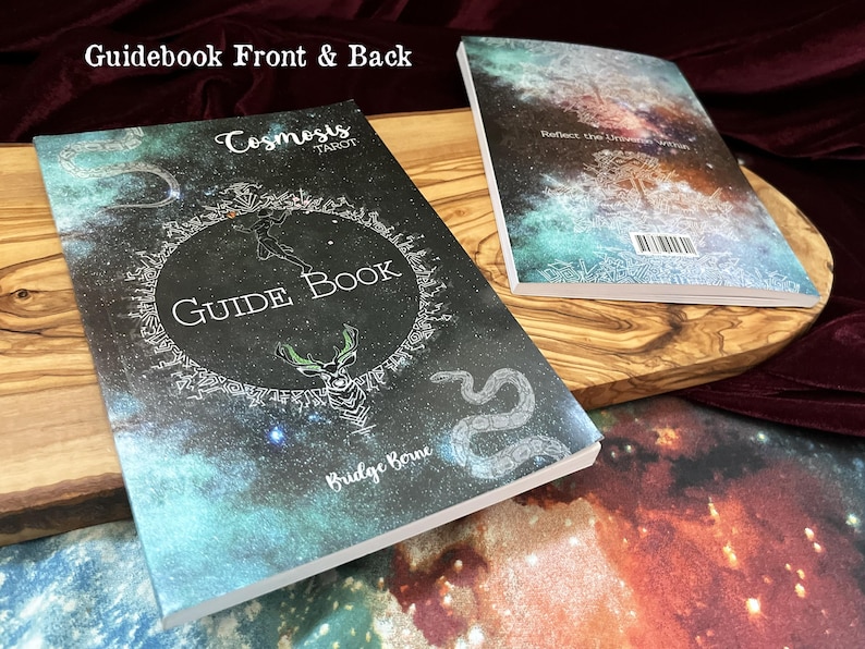 May include: Two paperback guidebooks for the Cosmosis Tarot deck, showing front and back covers. The covers feature a dark space-themed background with nebula colors, a central circular emblem, a deer head, a snake, and the text Guide Book.