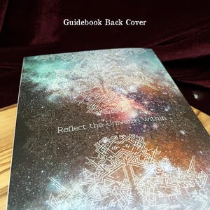 May include: A rectangular guidebook back cover featuring a dark space-themed background with nebula colors of teal, orange, and purple. The cover displays white geometric line art patterns and the text "Reflect the Universe within" in white.