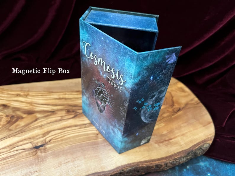 May include: A rectangular magnetic flip box featuring a deep blue and purple galaxy print. The front displays the text "Cosmosis TAROT" in white script and block lettering, accompanied by a central anatomical heart illustration and small blue butterflies.