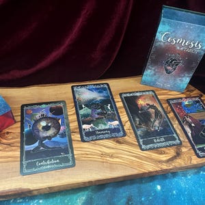 May include: A Cosmosis Tarot deck featuring a box with a heart illustration and four cards laid out. The cards are titled Contribution, Harmony, Rebirth, and Responsibility, each displaying colorful, celestial-themed artwork with dark borders.