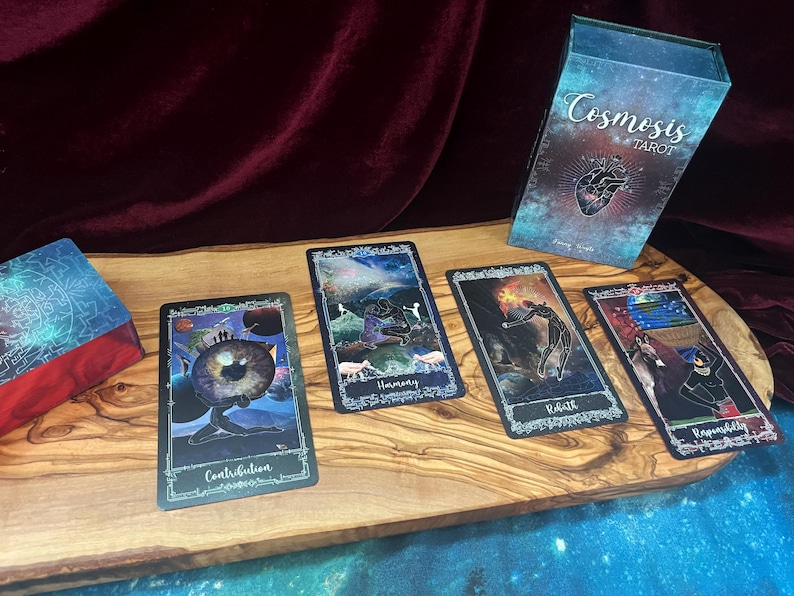 May include: A Cosmosis Tarot deck featuring a box with a heart illustration and four cards laid out. The cards are titled Contribution, Harmony, Rebirth, and Responsibility, each displaying colorful, celestial-themed artwork with dark borders.