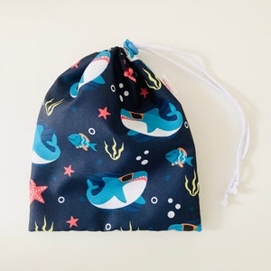 Wasserdichte Tasche für nasse Badeanzüge aus marineblauem, wasserdichtem Stoff mit Haimuster und Brille.