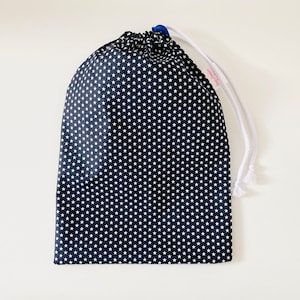 Könnte beinhalten: Eine schwarze Kordeltasche mit weißen Sternen bedruckt. Die Tasche hat eine weiße Kordel und einen blauen Besatz.
