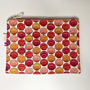May include: A rectangular zippered pouch with a repeating pattern of red, orange, and yellow seashells on a white background. The zipper is silver, and a small tag with red, white, and blue stripes is attached.