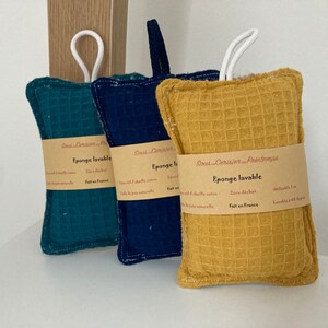 May include: Three rectangular, textured, washable sponges in green, blue, and yellow. Each sponge has a white loop handle and a label that reads "Eponge lavable" and "Sous Cerisier Printemps".