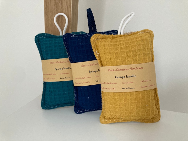 May include: Three rectangular, textured, washable sponges in green, blue, and yellow. Each sponge has a white loop handle and a label that reads "Eponge lavable" and "Sous Cerisier Printemps".