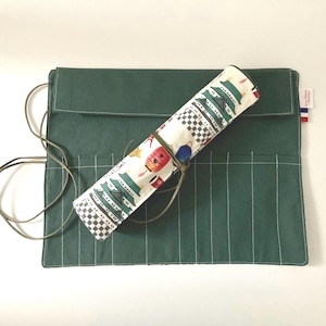 Peut inclure: Un étui enroulable en toile verte avec une doublure en tissu blanc arborant un motif d'inspiration japonaise. L'étui comporte plusieurs fentes pour ranger des outils ou des fournitures.