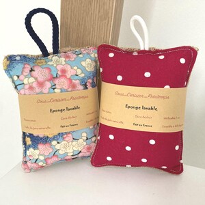 May include: Two handmade, washable sponges with a hessian backing. One sponge is red with white polka dots and the other is blue with a floral pattern. Both sponges have a brown label that reads "Sous Cerisier Printemps" and "Eponge lavable" in French. The label also says "Zero dechet" and "Fait en France".
