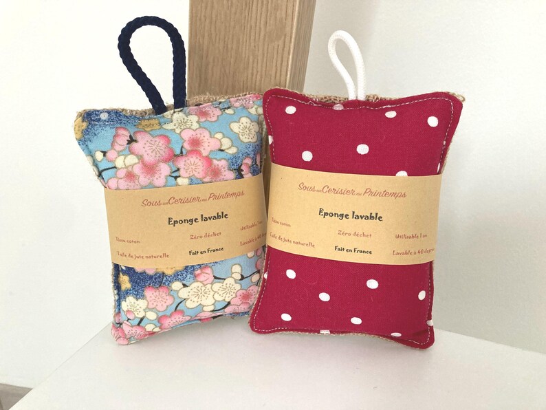 May include: Two handmade, washable sponges with a hessian backing. One sponge is red with white polka dots and the other is blue with a floral pattern. Both sponges have a brown label that reads "Sous Cerisier Printemps" and "Eponge lavable" in French. The label also says "Zero dechet" and "Fait en France".