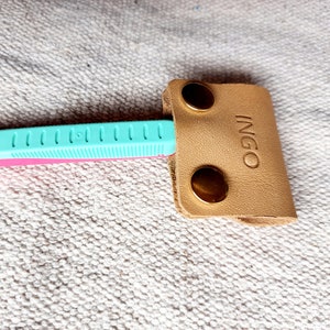 May include: A light tan leather razor cover with the embossed word "INGO" and two brass-colored snap closures. The cover is protecting a pink and teal razor.