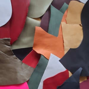 May include: A collection of irregularly shaped leather scraps in various colors, including red, black, green, orange, and white. The pieces are arranged closely together, creating a textured and colorful display. The leather appears to have a slightly worn or distressed look.