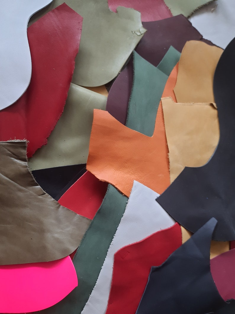 May include: A collection of irregularly shaped leather scraps in various colors, including red, black, green, orange, and white. The pieces are arranged closely together, creating a textured and colorful display. The leather appears to have a slightly worn or distressed look.