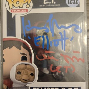 May include: A Funko Pop! vinyl figure of E.T. the Extra-Terrestrial and Elliott from the movie E.T. The figure is in its original packaging, with the words "Elliott & E.T." and "Vinyl Figure" printed on the box. The box is signed in blue and red marker.