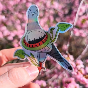 Pode incluir: Um adesivo holográfico de um desenho animado de um pombo usando um salva-vidas de melancia. O pombo é cinza com bico vermelho e pés vermelhos. A melancia é verde com sementes vermelhas. O adesivo está sobre um fundo rosa e branco.