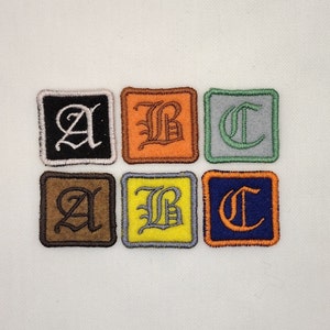 May include: Six embroidered fabric patches with the letters A, B, and C in a gothic font. The patches are in different colors: black, brown, orange, yellow, green, and blue.