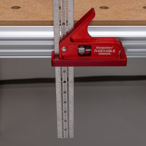 May include: A red Woodpeckers in-DEXABLE measuring tool with a ruler and protractor. The tool is mounted on a wooden surface.