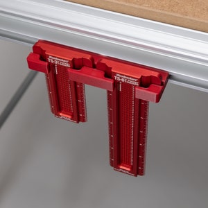 Könnte beinhalten: Zwei rote Woodpeckers TS-3F und TS-6F Taschenwinkel sind an einer silbernen Schiene befestigt. Die Winkel haben eine rote, strukturierte Oberfläche mit weißen Markierungen und schwarzem Text.