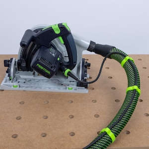 May include: A black and green circular saw with a dust collection hose attached to a workbench. The hose is secured with green clips. The saw is labeled "FESTOOL".