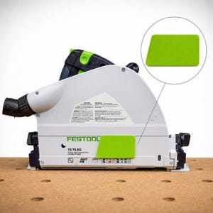 Könnte beinhalten: Eine Festool TS 75 EQ Tauchsäge mit weißem Gehäuse und schwarzen sowie hellgrünen Akzenten. Die Seite zeigt Sicherheitshinweise, den Markennamen und einen kreisförmigen Ausschnitt, der ein hellgrünes rechteckiges Bauteil hervorhebt.