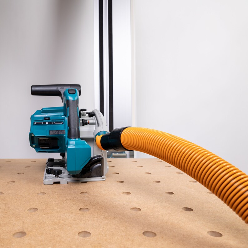 May include: A teal and black circular saw with a dust collection hose attached. The saw is on a wooden surface with holes.