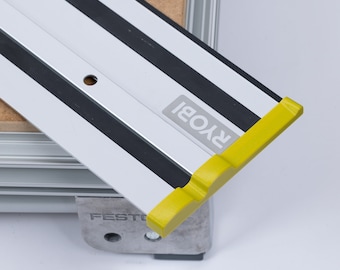 May include: A silver and black guide rail with a yellow plastic end cap. The rail has the word "RYOBI" printed on it. The rail is attached to a silver metal base with the word "FESTO" printed on it.