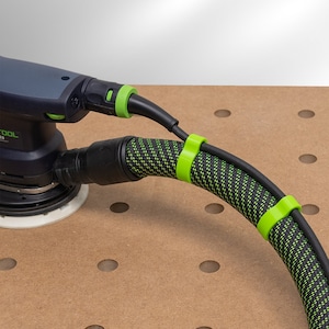May include: A black and green power tool with a black hose attached to it. The hose is secured with green clips. The tool is sitting on a brown pegboard.