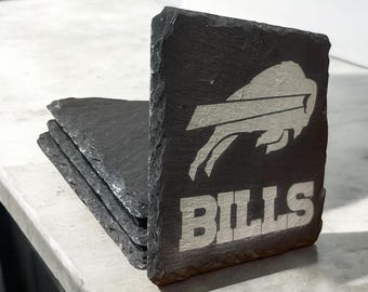 May include: A set of four black slate coasters featuring a white Buffalo Bills logo and the word "BILLS" printed on the front.