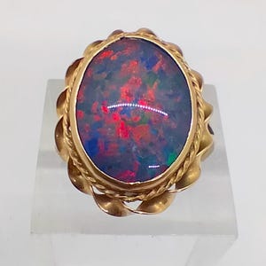 May include: A gold ring featuring an oval black opal gemstone set in a twisted gold band.