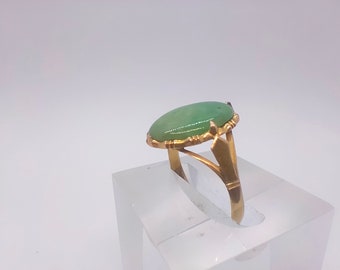 May include: A gold ring with a green oval gemstone set in a gold bezel. The ring has a delicate, intricate design.