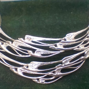 May include: A silver necklace with a delicate chain and a large, intricate pendant. The pendant is made of multiple layers of silver that are woven together to create a unique and organic design.
