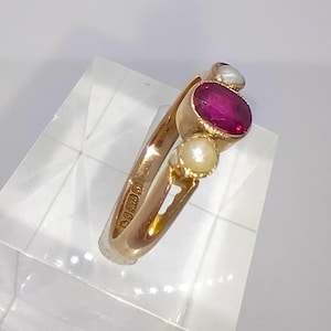 Pode incluir: Um anel de ouro com uma pedra vermelha e três pérolas brancas. O anel é marcado com "9ct 375".