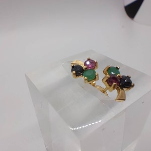 May include: A pair of gold earrings with a cluster of three gemstones. The gemstones are green, pink, and black.
