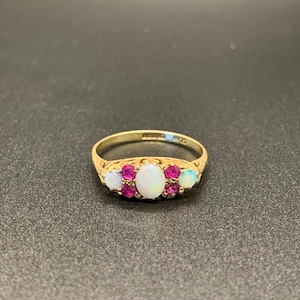 Op de afbeelding: Een gouden ring met een witte opaal en roze robijnen, gezet in een delicaat bloemmotief.